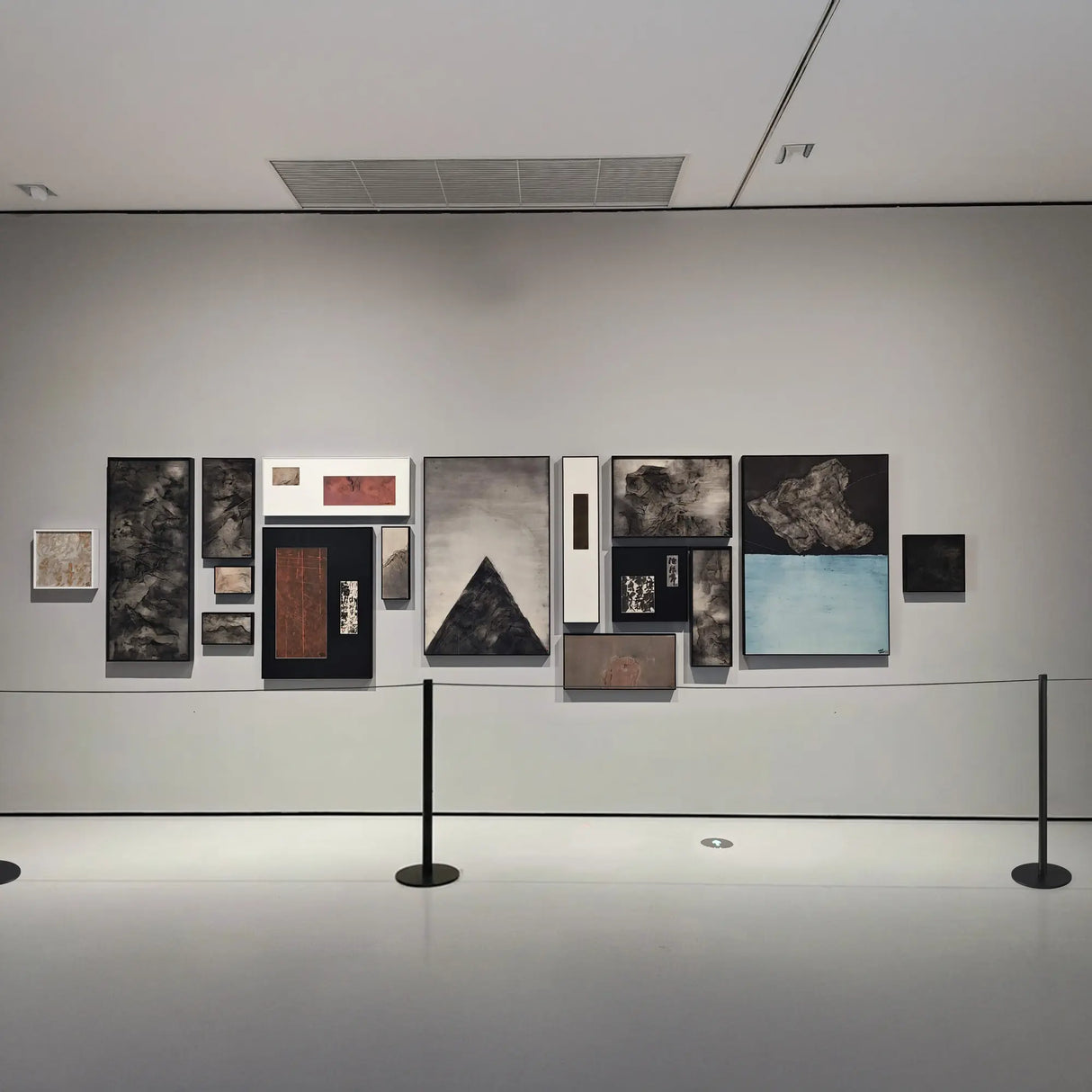 Art gallery slim stanchions system with various framed artworks on a wall.