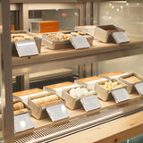 Acrylic megnetic display blocks with small white labels in front of each food item, Along with pastries and cookies on wooden shelves.