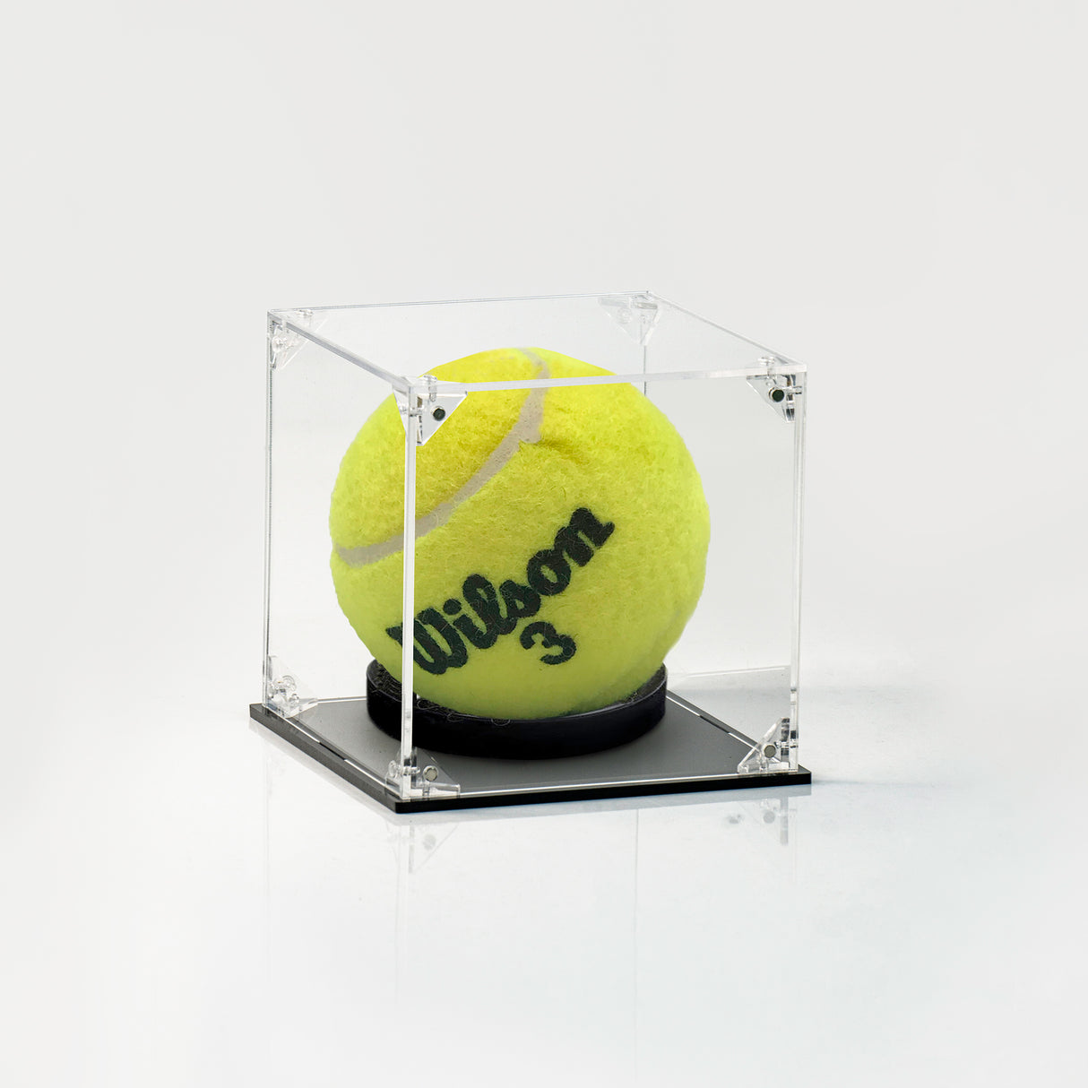 A yellow tennis ball with 'Wilson 3' printed on it, displayed inside a clear acrylic cube case with a black base on a white background.