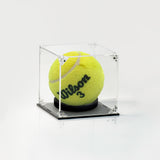 A yellow tennis ball with 'Wilson 3' printed on it, displayed inside a clear acrylic cube case with a black base on a white background.